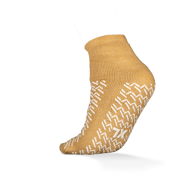 Pictured is a single mustard yellow ECO-PLUS anti-slip disposable sock, double-sided coated by AMPri Handelsgesellschaft mbH, on a white background, with white non-slip grips and ideal for medical areas.