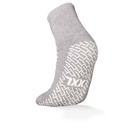 Pictured is a single gray ECO-PLUS anti-slip disposable sock from AMPri Handelsgesellschaft mbH with a white anti-slip grip and "TXX" lettering on the sole. Double-sided coated, ideal for medical areas; the background is plain white.
