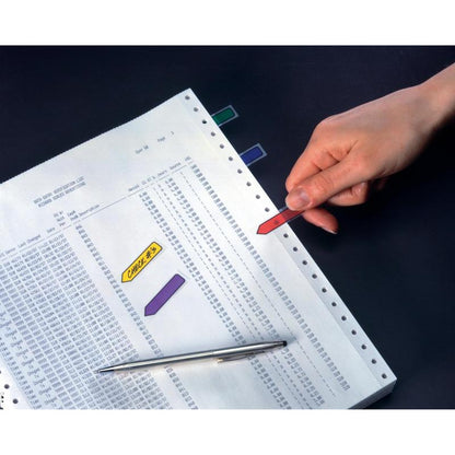 A hand holds a 3M Post-it® Index Arrow (11.9 mm x 43.2 mm, various colors) over a data printout; more sticky notes and a pen lie on the perforated sheet, all on a dark surface - ideal for organizing documents.
