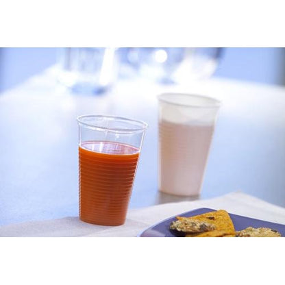 A Starpak 100 drinking cup, PP, white by Starpak is filled with a red liquid and stands in front of a white cup with a light drink. Crackers are on a plate in front of it, ideal for events. The background appears blurry.