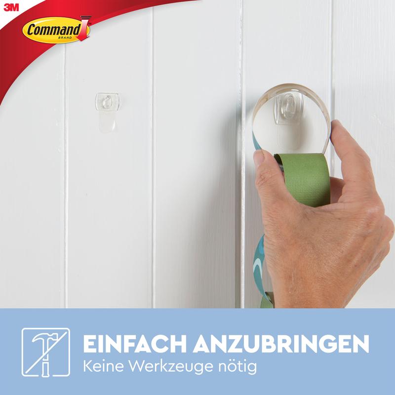 A hand attaches a Command™ Mini Hook, transparent, from 3M Deutschland GmbH to a white wooden wall. Text: "Easy to apply. No tools needed. Remove without a trace with transparent strips (17006CLR).