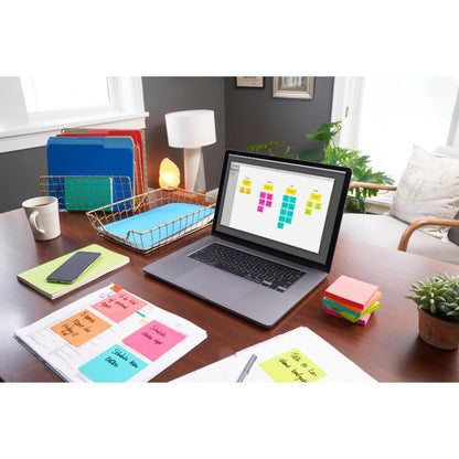 A desk with a laptop, on which a sticky note organizer, Post-it® Notes (76 mm x 76 mm, 100 sheets/block, 100% PEFC) from 3M Deutschland GmbH, binders, paperwork, a phone, a lamp, a plant, and sunlight illuminate the organized workspace.