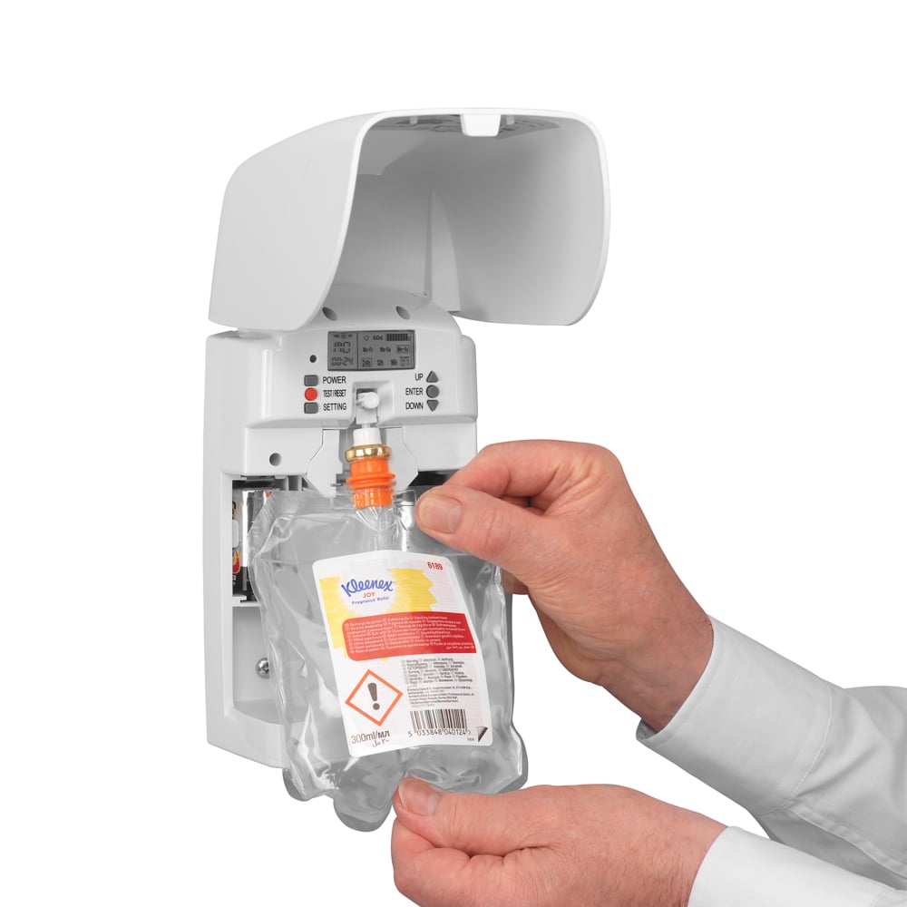 A person places a Kleenex® Joy Scent refill pack (300 ml, clear) from Kimberly-Clark GmbH into a white wall-mounted dispenser, ensuring long-lasting freshness with visible buttons and indicator lights.