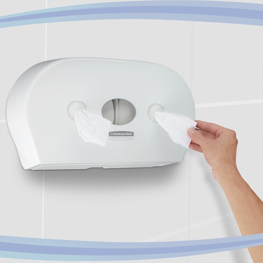 Eine Hand zieht Taschentücher aus einem Kimberly-Clark GmbH Aquarius™ Toilettenpapierspender - Zentralentnahme / Weiß / Jumbo, der mit zwei Rollen ausgestattet und an einer gefliesten Wand montiert ist.