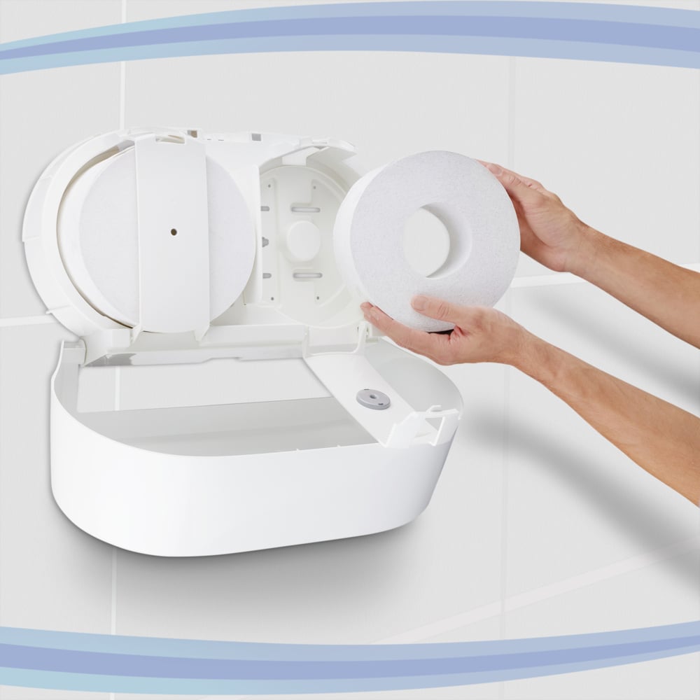 Eine Person belädt einen Kimberly-Clark GmbH Aquarius™ Toilettenpapierspender - Zentralentnahme / Weiß /Jumbo-, mit geöffnetem Deckel. Die weiß gefliesten Wände und die blauen Kurven im Hintergrund unterstreichen das praktische zentrale Spenderdesign.