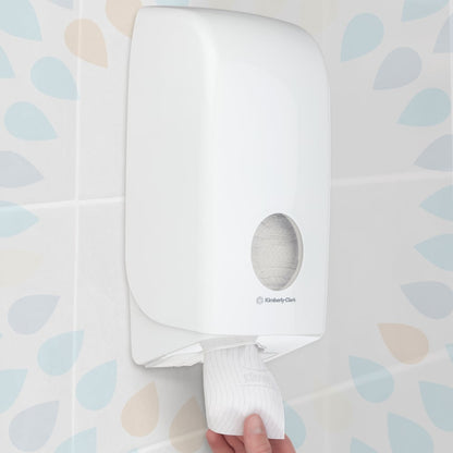 A hand pulls a sheet from a wall-mounted Kleenex® toilet paper single sheet system (Kimberly-Clark GmbH), white, 200 sheets per pack, 36 packs, in a bathroom with patterned tile walls.