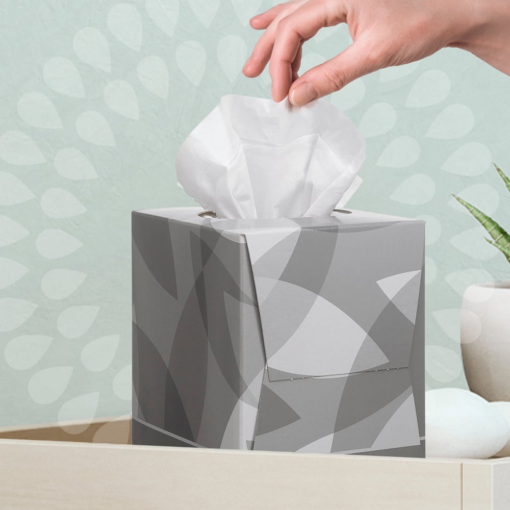 A hand pulls a Kleenex® facial tissue - cube box / white from Kimberly-Clark GmbH from a bright surface, near which a plant and decorative stones are located - ideal for your facial care routine.