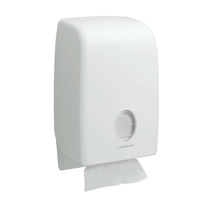 A white, wall-mounted Kimberly-Clark Scott® Essential™ hand towel dispenser with a round window shows interfold towels inside (White, Small, 15 clips x 340 sheets) and a towel partially dispensed for hygienic hand drying.