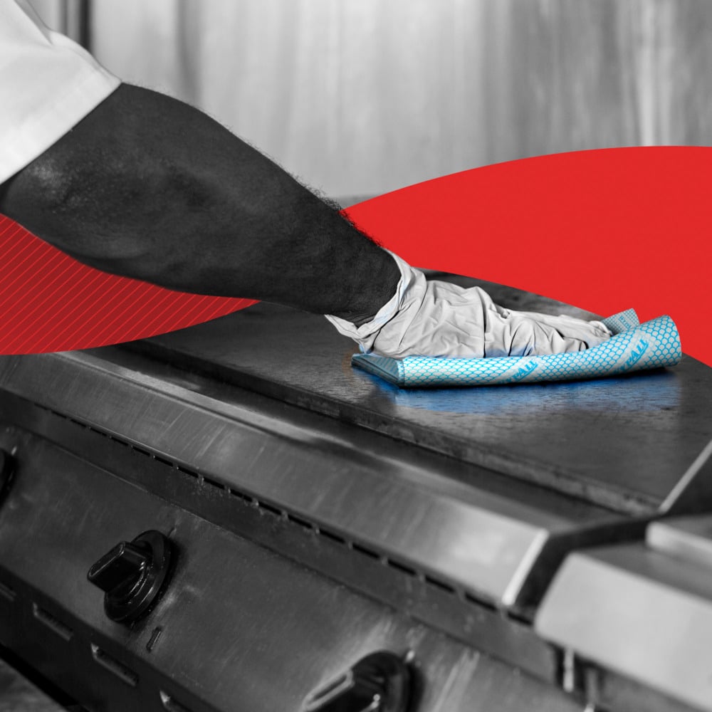 Eine Person mit Handschuhen wischt eine Metallherdplatte mit einem blauen WypAll® X50 Wischtücher - Interfold Tuch (41,80 cm x 24,70 cm) der Kimberly-Clark GmbH. Eine rote geschwungene Grafik im Hintergrund unterstreicht die Sauberkeit und Pflege der Küche.