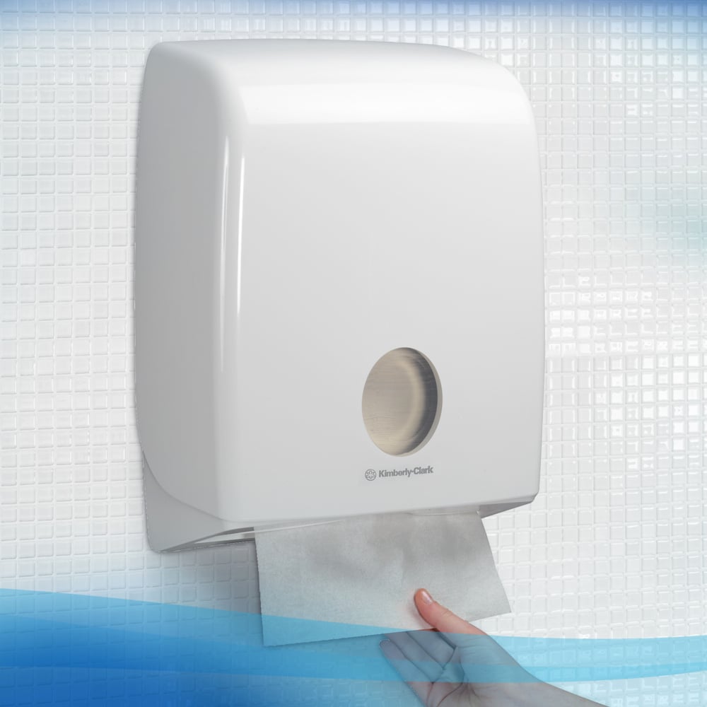 A hand pulls a Scott® Control™ folded towel from Kimberly-Clark GmbH out of a white wall dispenser with a round viewing window against a white-blue tiled background. Packaged: 15 clips x 240 sheets per carton (15 packs).