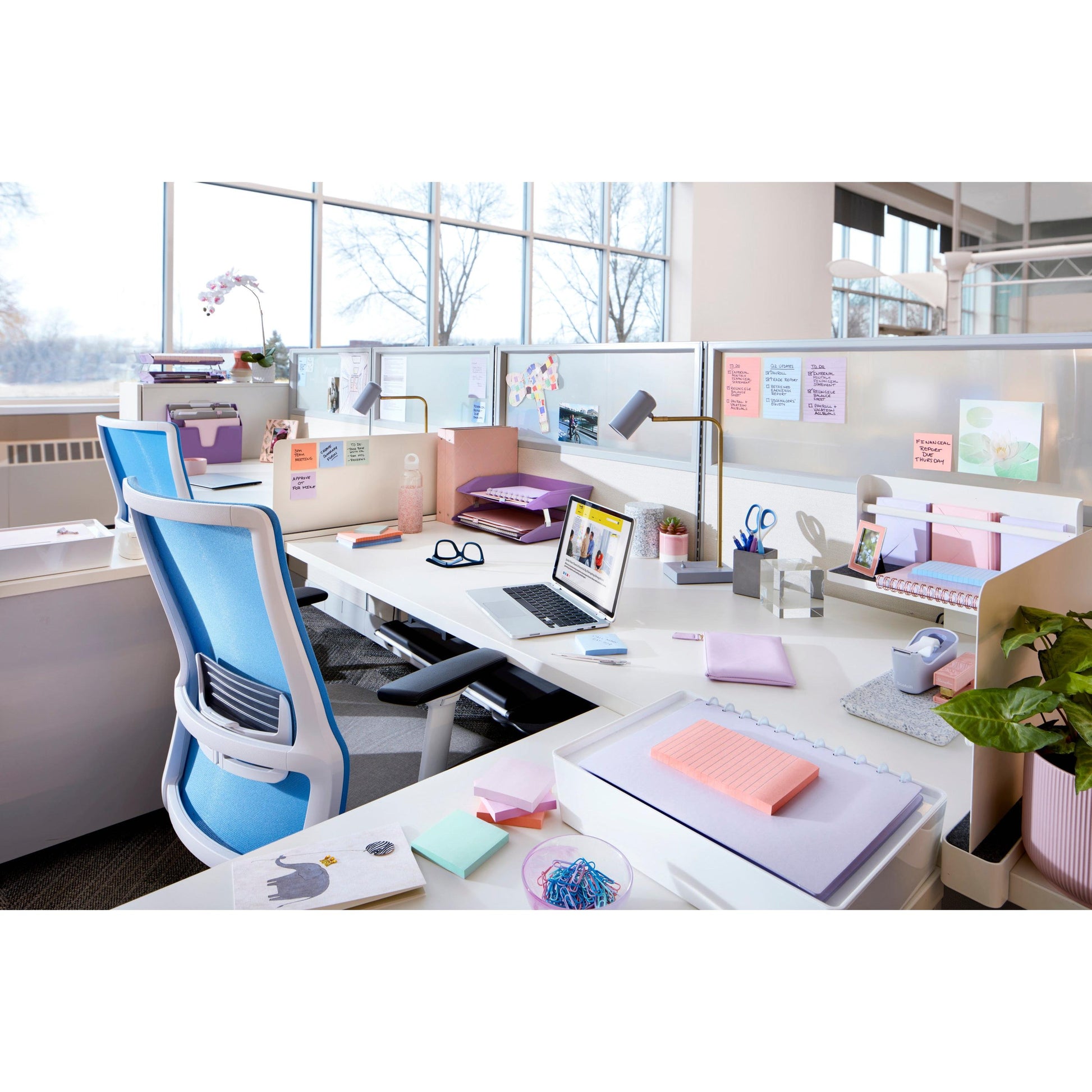 Ein modernes Büro mit weißen Schreibtischen, blauen ergonomischen Stühlen, Laptops, Verbrauchsmaterialien, persönlichen Gegenständen, Topfpflanzen und Post-it® Super Sticky Notes (76x76 mm, 90 Blatt/Block, 100% PEFC) von 3M Deutschland GmbH an den Trennwänden; draußen eine verschneite Landschaft.