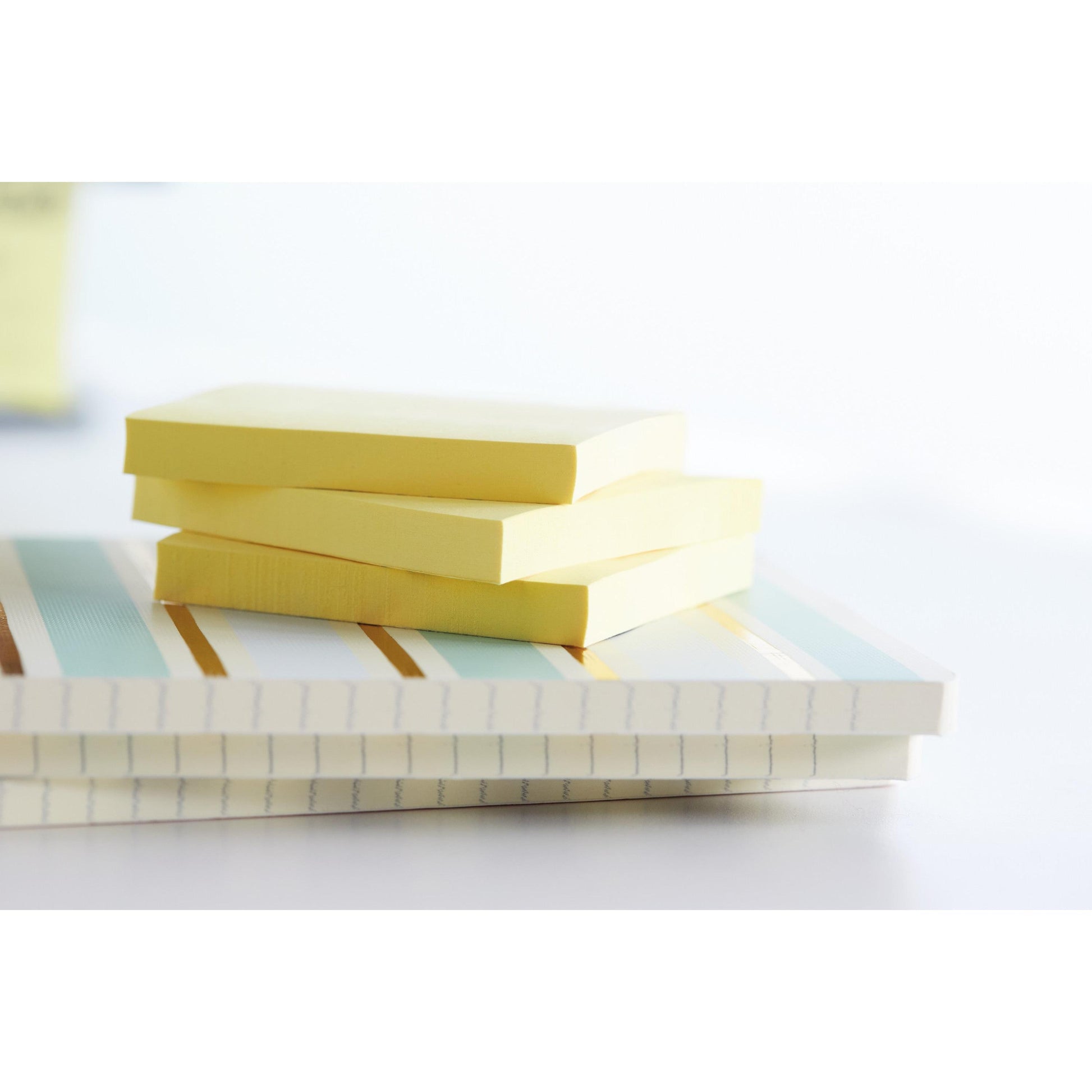 Drei Stapel Post-it® Recycling Z-Notes (76x76 mm, 100 Blatt/Block, 100% PEFC) der 3M Deutschland GmbH ruhen auf zwei gestreiften Notizbüchern in hellem Licht mit einem sanft verschwommenen Hintergrund.
