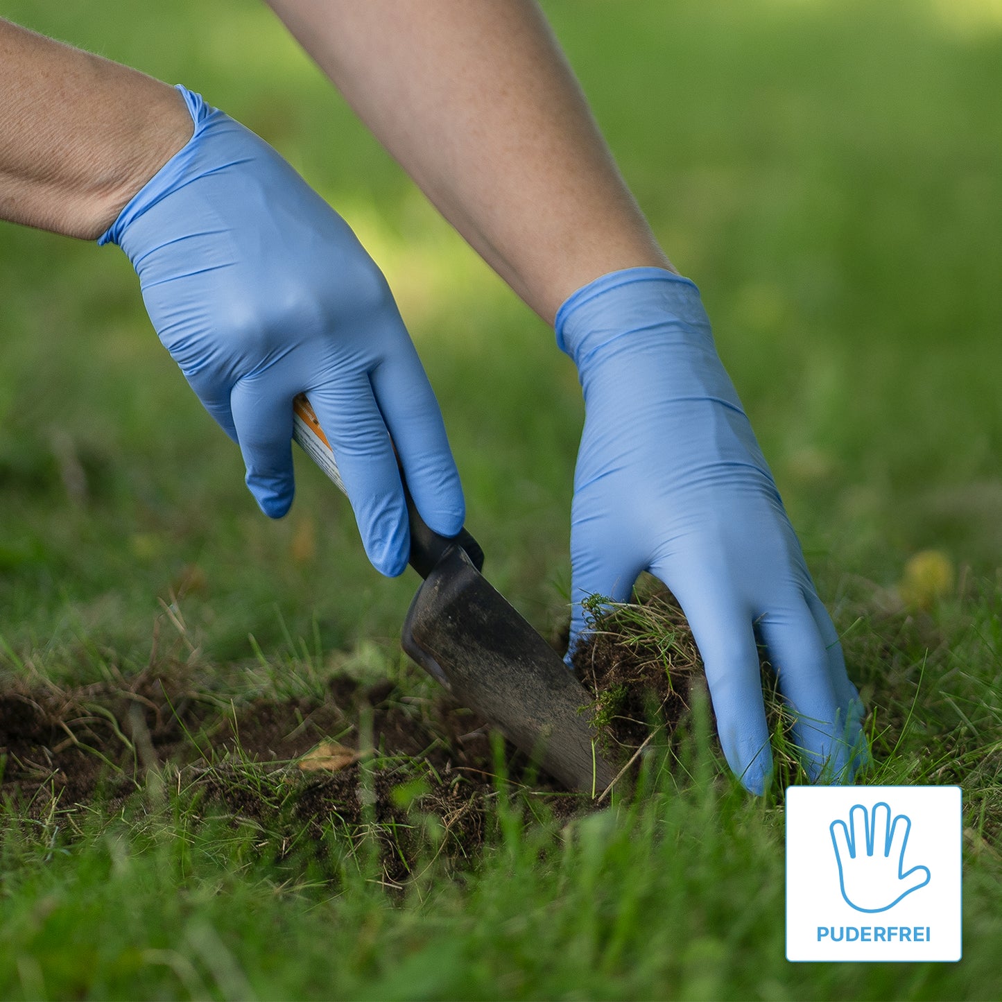 A person wearing ARNOMED NITRIL BLUE XTRA STRONG extra-thick disposable nitrile gloves from ARNOWA GmbH is using a hand trowel to dig up soil in a meadow. In the corner, there is a "powder-free" label featuring a glove symbol.