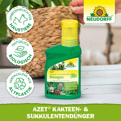 Eine grüne Plastikflasche von Neudorff Shop Azet Kakteen- & SukkulentenDünger flüssig steht auf einem Holztisch vor einem getopften Kaktus. Drei Symbole weisen darauf hin, dass es haustierfreundlich, biologisch und aus recyceltem Kunststoff hergestellt ist.