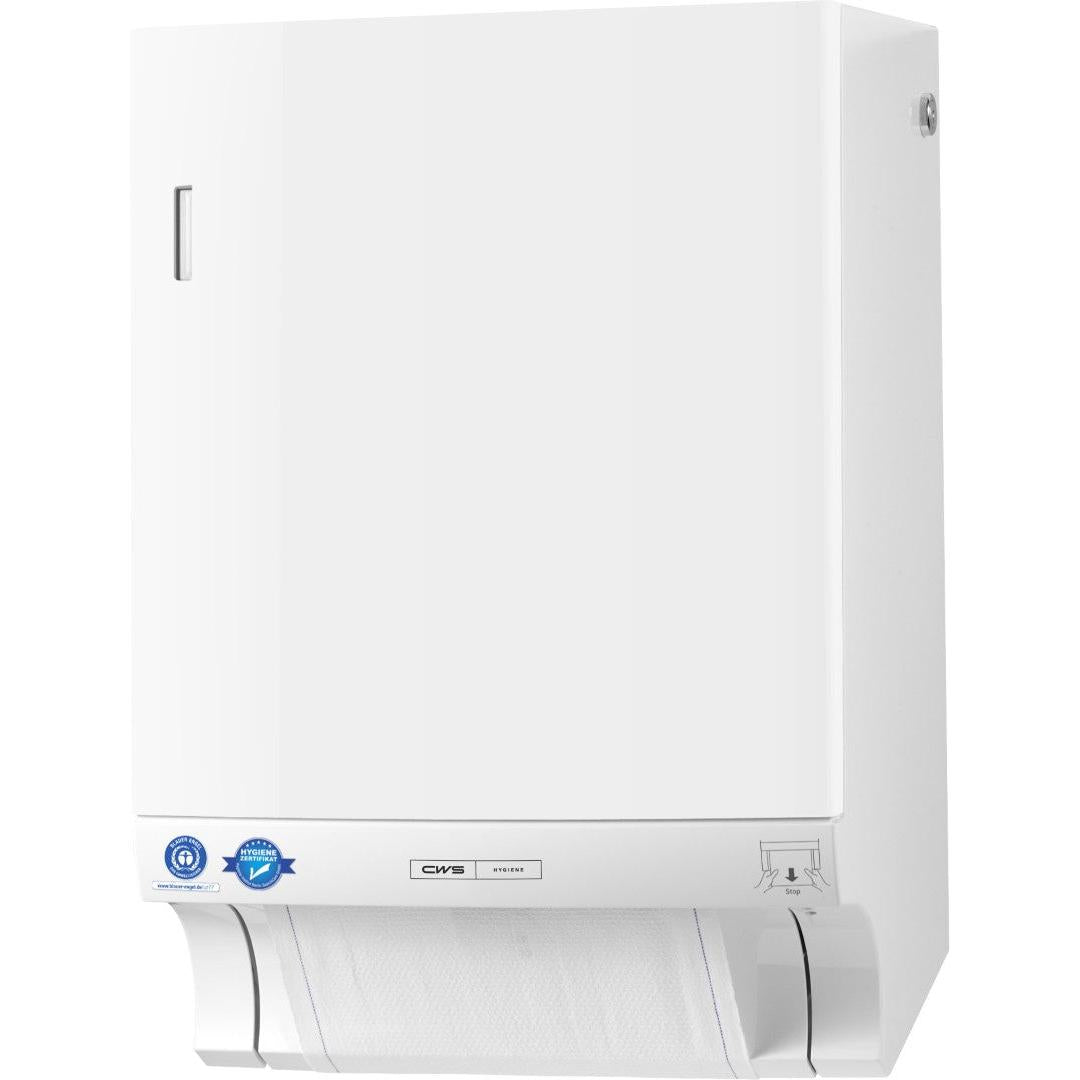 A white CWS ParadiseLine fabric towel dispenser Dry Slim including panel with a slim design is mounted on the wall and shows a partially extracted sheet at the bottom. Blue stickers, a small silver label, and an illustrated manual are located near the bottom.