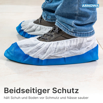 Person trägt ARNOMED CPE/PP Schuhüberzieher von ARNOWA GmbH, wasserdicht und in Blau-Weiß, über grauen Schuhen auf hellen Fliesen; Text und Branding sind sichtbar.