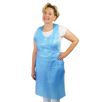 A person is standing smiling with one hand on their hip, wearing an ARNOMED COVER PE-APRON Blocked Disposable Apron made of PE (18µ thickness) by ARNOWA GmbH over a white shirt and white pants against a plain white background.