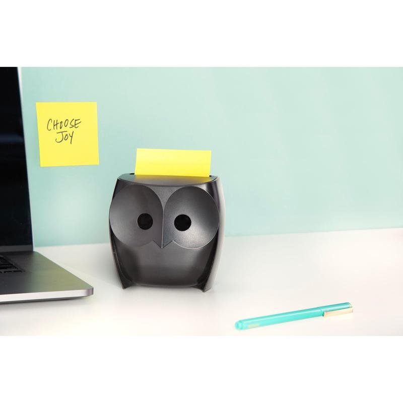 Ein schwarzer Post-it® Z-Zettelspender "Eule" (3M Deutschland GmbH) mit gelben Super Sticky Z-Zetteln steht auf einem weißen Schreibtisch, daneben ein Laptop und ein blauer Stift. An der Wand hängt ein "CHOOSE JOY"-Zettel vor hellblauem Hintergrund.