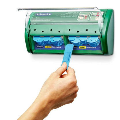 A hand pulls a bandage out of a green Salvequick X-ray-detectable bandage dispenser (Orkla Wound Care AB) containing 2x30 plaster refills, with additional bandages visible inside the dispenser.