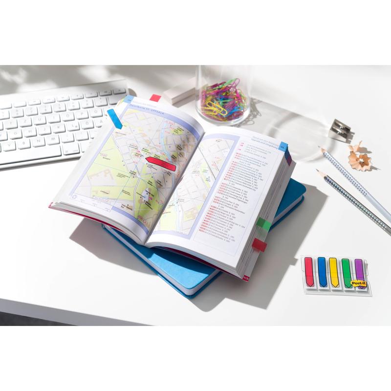 An open card book with colored tabs lies on a blue notebook on a white desk next to office supplies and 3M Post-it® Index Arrows (11.9 mm x 43.2 mm, 100 sticky notes/dispenser) - perfect for organizing documents and marking pages.
