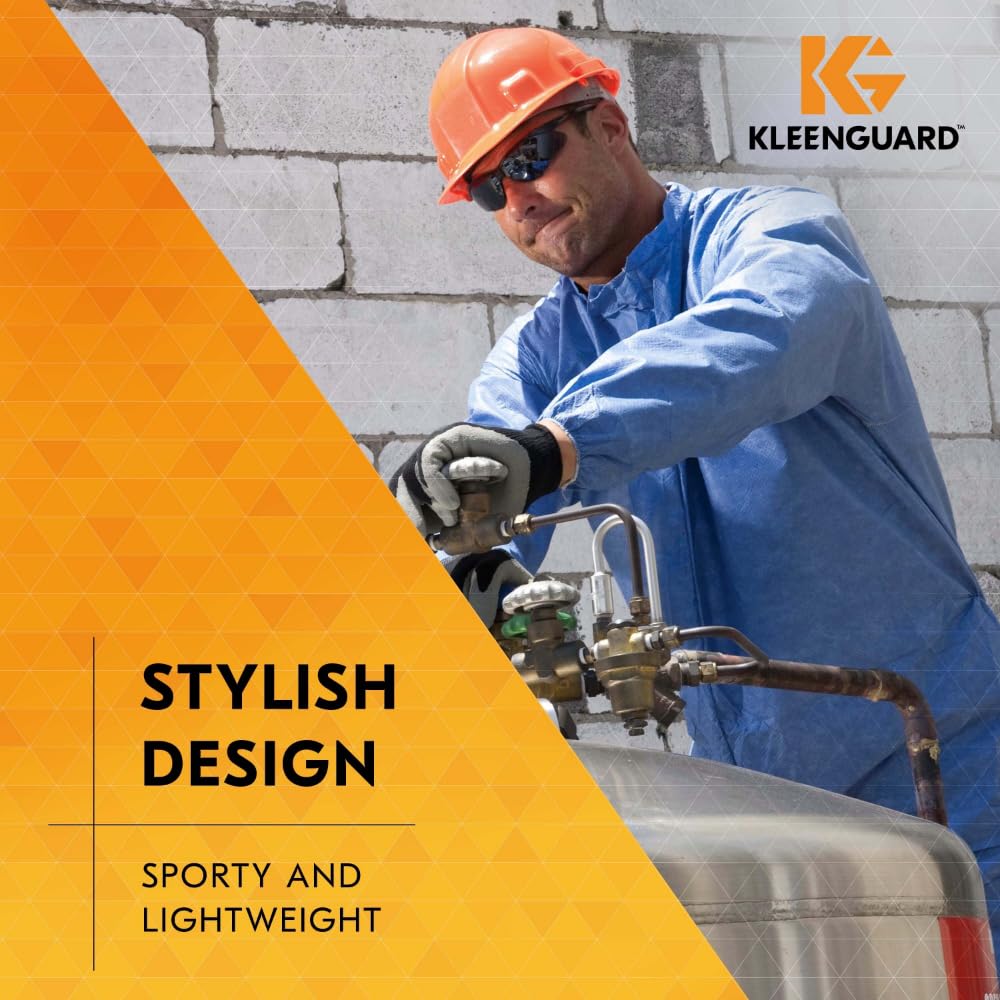 Eine Person in einem blauen Schutzanzug mit Handschuhen, Sonnenbrille und orangefarbenem Schutzhelm bedient Maschinen an einer Betonwand. Die Kimberly-Clark GmbH KleenGuard® V30 Nemesis™ Schutzbrille Smoke Spiegel bietet eleganten, leichten und kratzfesten Augenschutz.