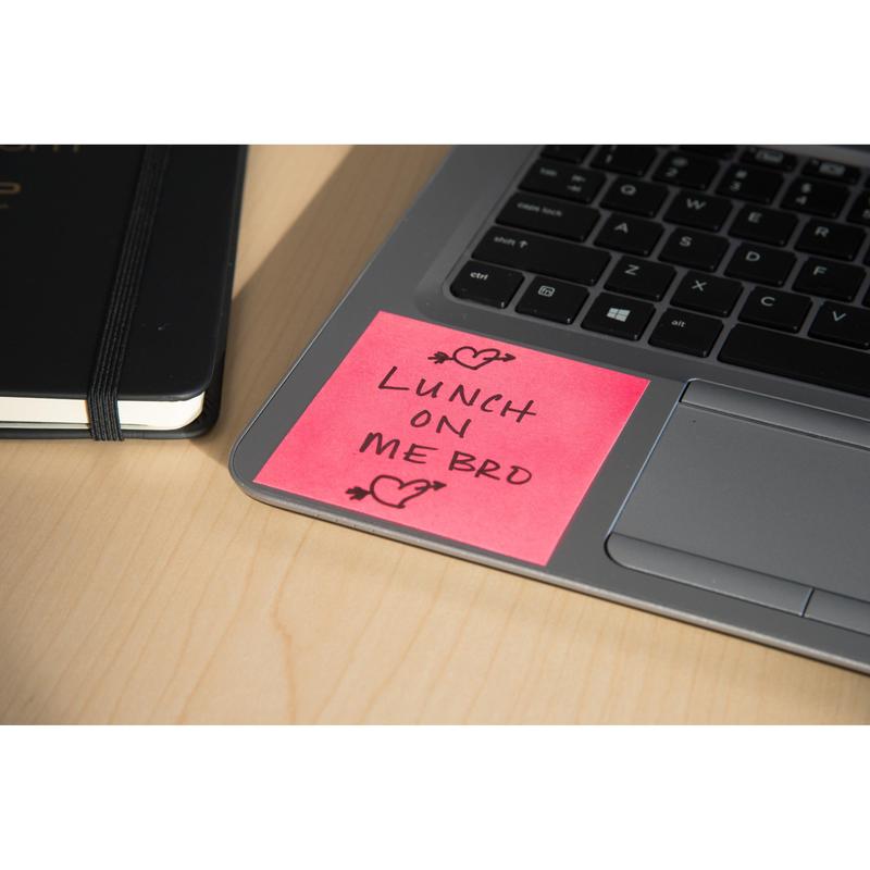 A Post-it® Notes cube (76x76mm, 450 sheets, 100% PEFC) from 3M Deutschland GmbH in pink sits on a laptop keyboard with "LUNCH ON ME BRO" and heart doodles. A closed black notebook lies next to it on a light wooden table.