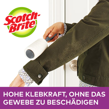 Eine Person entfernt mit dem Scotch-Brite™ Everyday Clean Fusselroller, 30 Blatt von 3M Deutschland GmbH, Fusseln von einer dunkelgrünen Jackenärmel. Text: "Hohe Klebkraft, ohne das Gewebe zu beschädigen.