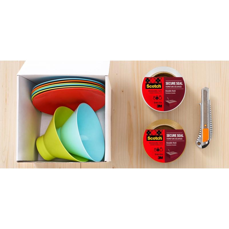 A box with colorful plates and bowls stands next to two rolls of Scotch® packaging tape for a secure seal (50 mm x 66 m) from 3M Deutschland GmbH, one clear and one brown, along with a utility knife on a light wooden surface.