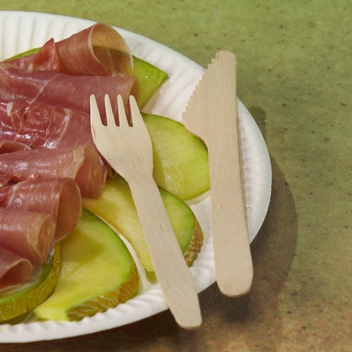 On a green speckled surface, green apple slices and folded prosciutto lie on a white plate, accompanied by PAPSTAR wooden forks "pure" 16.5 cm - eco-friendly and sturdy from PAPSTAR GmbH (25 pieces).