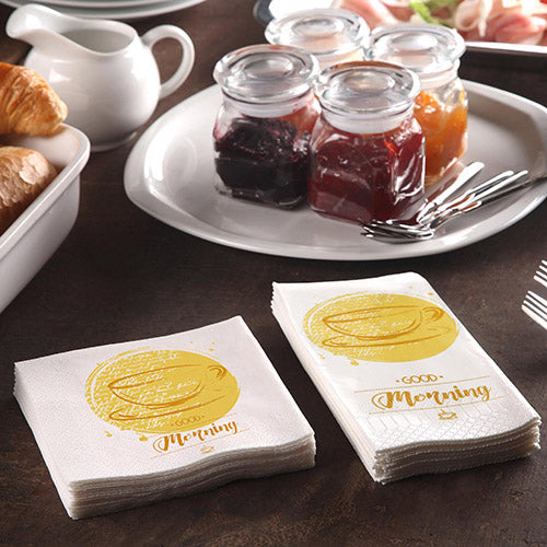 Ein Frühstückstisch mit Croissants, einer Kanne und 200 PAPSTAR Servietten (3-lagig 1/4-Falz, 24x24 cm) der PAPSTAR GmbH mit der Aufschrift „Guten Morgen“, dazu Marmeladengläser und drei Gabeln für ein gemütliches Morgenessen.