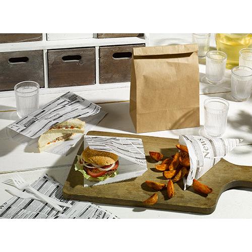 A sandwich, a burger at PAPSTAR "Newsprint" parchment-style hamburger bags (16x18 cm, 300 pieces) and potato wedges are on a wooden board. Next to them on the table are clear cups, white cutlery, and a brown paper bag. Brand: PAPSTAR GmbH.