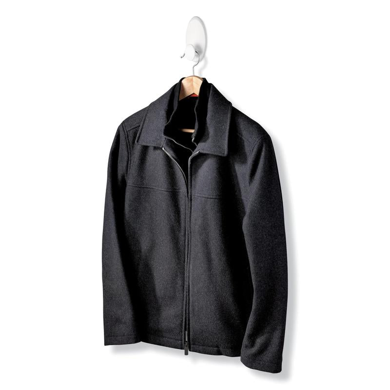 Eine schwarze Jacke mit Reißverschluss und Kragen hängt an einem Holzbügel des Command™ Kleider-Hakens, 17019-FGN, der eine Wandbefestigung ohne Bohren ermöglicht, vor einem schlichten weißen Hintergrund.