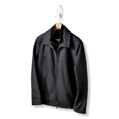 Eine schwarze Jacke mit Reißverschluss und Kragen hängt an einem Holzbügel des Command™ Kleider-Hakens, 17019-FGN, der eine Wandbefestigung ohne Bohren ermöglicht, vor einem schlichten weißen Hintergrund.