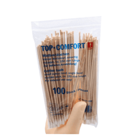 A hand is holding a clear plastic package of AMPri TOP-COMFORT cotton swabs, perfect for hospital care. The package contains 100 disposable cotton swabs with natural wood sticks; product details are provided in both German and English.