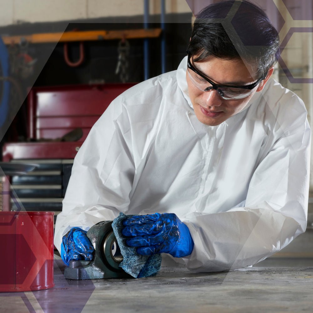 In a white suit, with blue gloves and safety goggles, a person kneels on the floor using Kimtech® process wipes - large roll (blue) from Kimberly-Clark GmbH, to clean a mechanical part in an industrial cleaning.