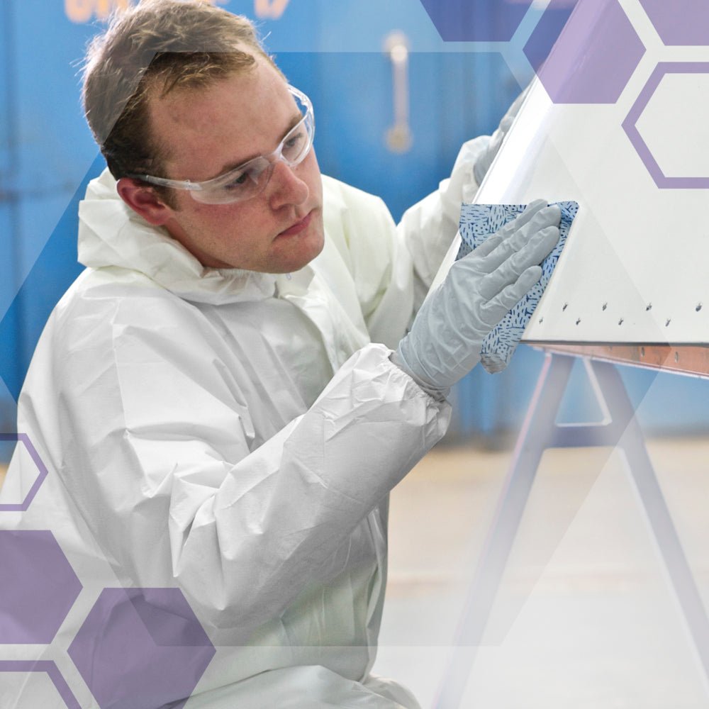A person in protective clothing uses a Kimtech® process wipes large roll (Kimberly-Clark GmbH) to clean a large white object in an industrial setting. A purple hexagon graphic overlays the image.