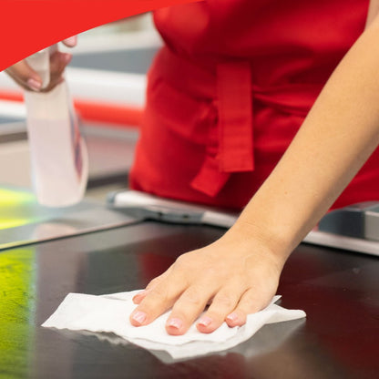 A person with a red apron cleans a countertop with a cloth from the WypAll® X50 General Clean large roll (1 roll x 1100 sheets) from Kimberly-Clark GmbH and holds a spray bottle for efficient surface cleaning in their hand.