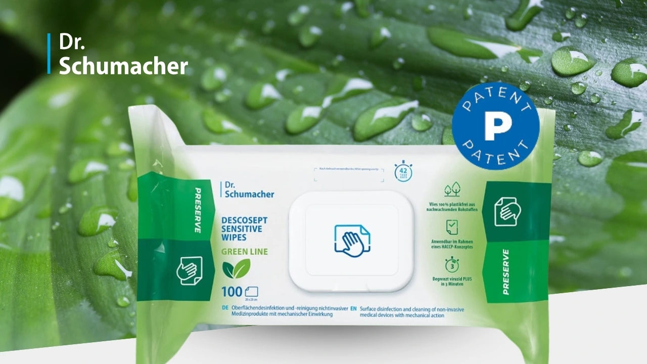 Produktbild von Dr. Schumacher: Vor einem grünen Blatt mit Wassertropfen steht eine Packung „Descosept Sensitive Wipes Green Line“. Auf der Verpackung sind ein wiederverschließbarer Deckel, grüne Seitenelemente und mehrere Symbole für Nachhaltigkeit und Anwendung zu sehen. Rechts oben befindet sich ein blauer Kreis mit der Aufschrift „Patent“.