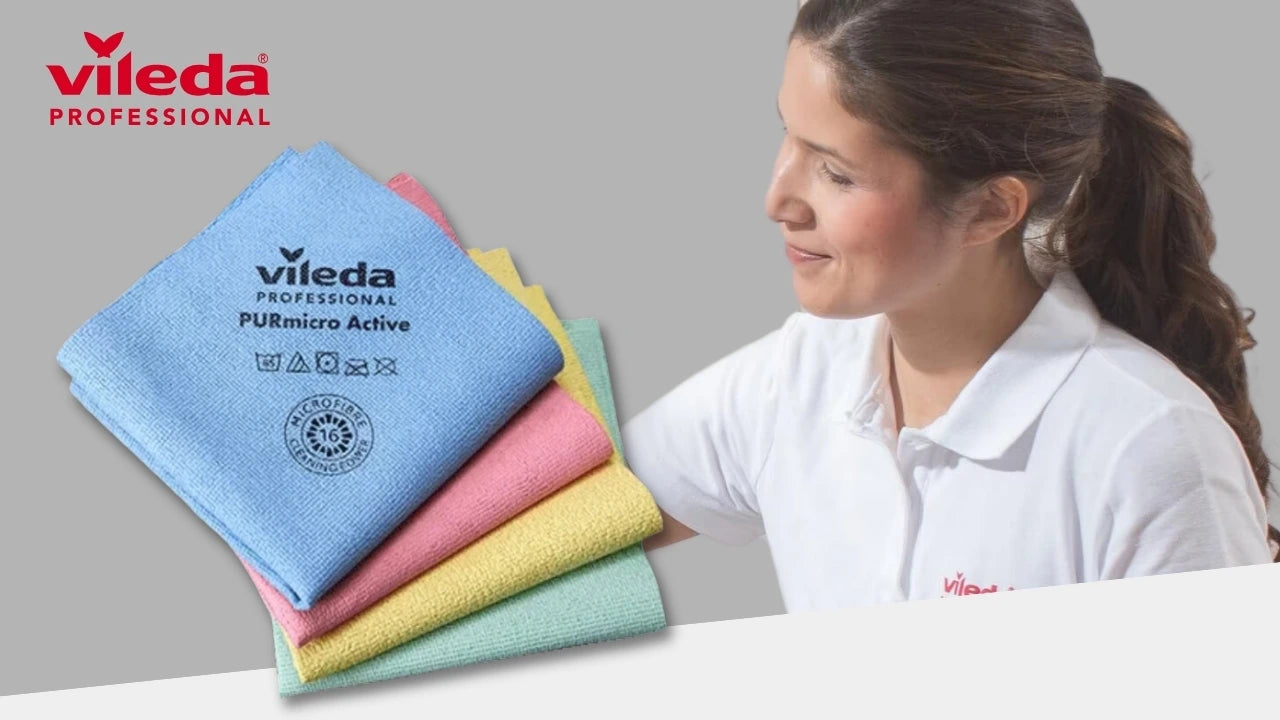 Werbebild von Vileda Professional mit vier farbigen Mikrofasertüchern (blau, rosa, gelb, grün) „PURmicro Active“ im Vordergrund; rechts lächelnde Frau im weißen Poloshirt mit Vileda-Logo vor grauem Hintergrund.