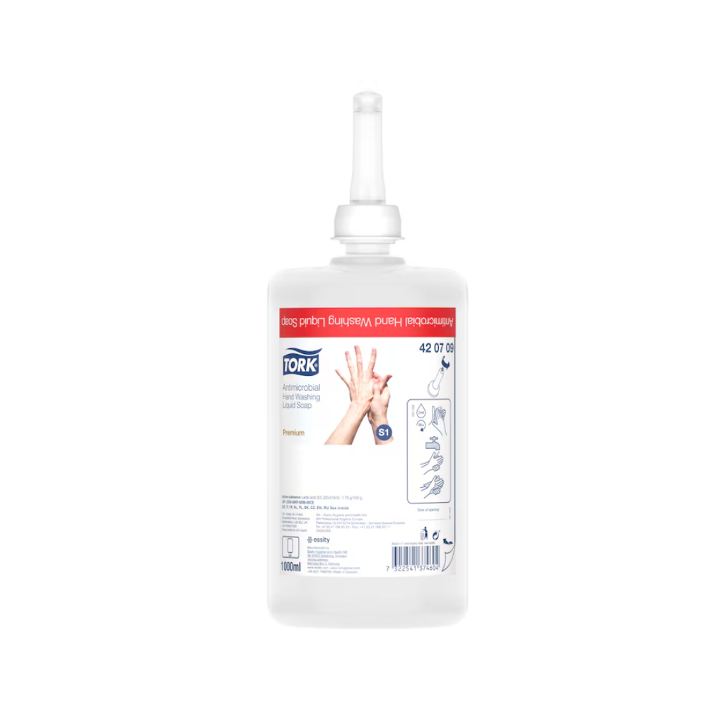 Pictured is a Tork liquid soap for hand decontamination refill bottle with a nozzle. The label shows usage instructions, the brand name TORK – Essity Professional Hygiene Germany GmbH, and product details. The transparent bottle reveals the liquid inside, emphasizing its use in food processing. The label is predominantly in red and white colors.