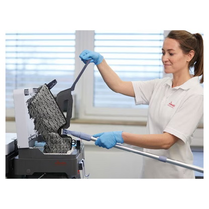 Eine Person mit blauen Handschuhen und weißem Hemd reinigt mit dem Vileda Professional Swep Duo r-MicroCombi Mop - 50 cm von Vileda GmbH eine strukturierte schwarze Oberfläche. Die Szene scheint in einem Innenbereich zu sein, mit einem großen Fenster im Hintergrund, durch das natürliches Licht in den Raum fällt.