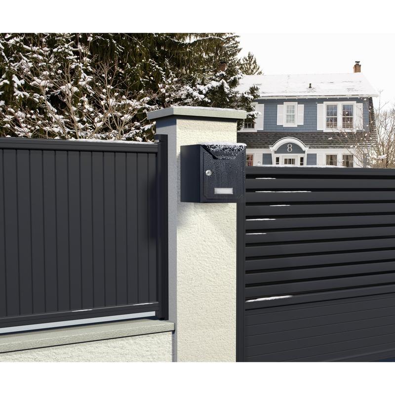 A modern black mailbox with snow is mounted on a white pillar next to a metal fence, secured with Scotch-FIX™ Extreme double-sided outdoor mounting tape from 3M Deutschland GmbH, with a blue-gray house and snowy trees in the background.