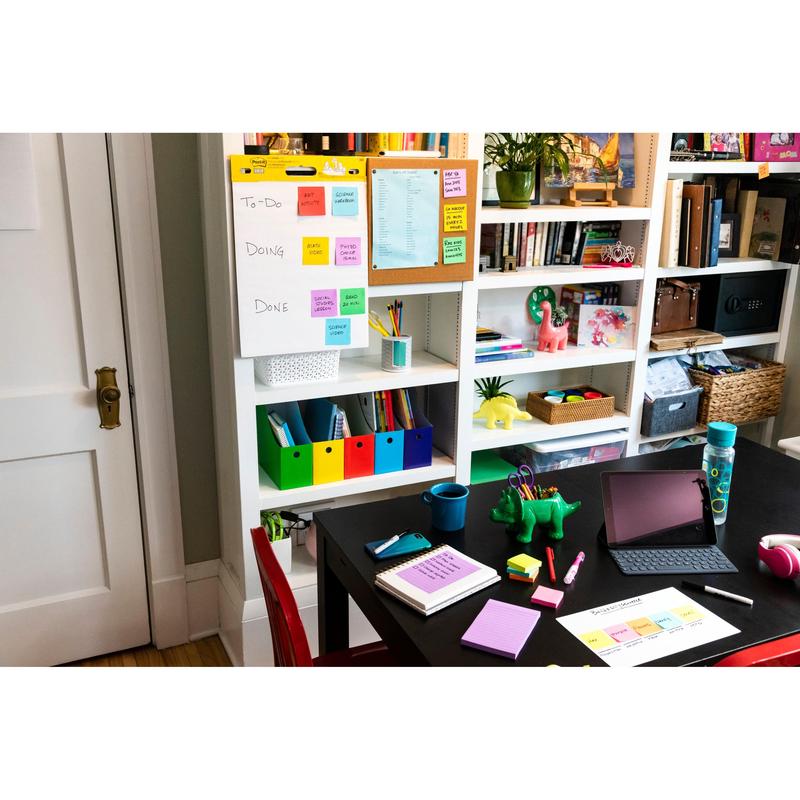 A home office with a black desk, a red chair, and shelves with books and storage space. On the desk are an iPad, notebooks, pens, a water bottle, a green dinosaur figure, and 3M Post-it® Super Sticky Notes (47.6x47.6mm, 90 sheets/block, 100% PEFC).