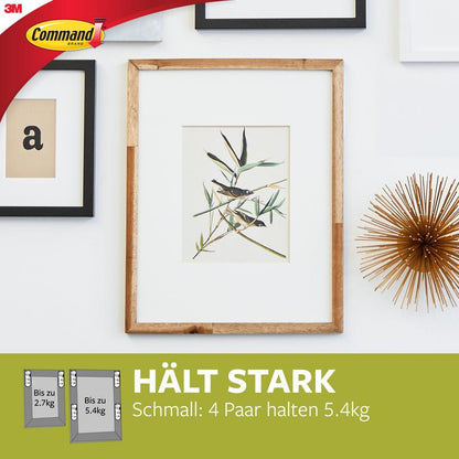 Ein gerahmter Pflanzendruck hängt an einer weißen Wand mit anderen Rahmen und einem Goldobjekt. Unten werden die Schmale Command™ Bilder-Montage Strips (M) 17207 der 3M Deutschland GmbH wegen ihrer rückstandslos entfernbaren und starken Haltekraft beworben.