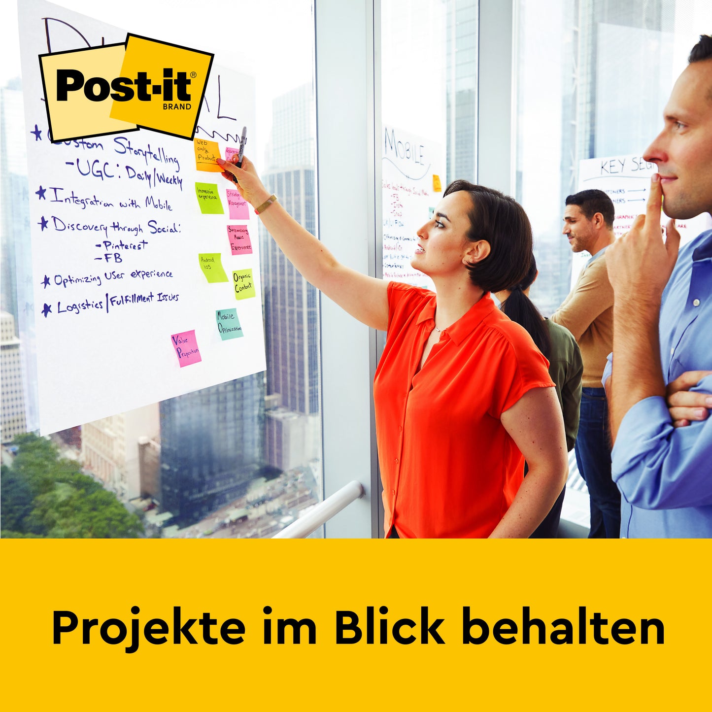 Eine Frau schreibt auf ein Post-it® Super Sticky selbsthaftendes Meeting Chart (58,4 x 50,8 cm, 20 Blatt) von 3M Deutschland GmbH, das an einer Bürowand montiert ist. Zwei Personen stehen daneben. Unten steht: "Projekte im Blick behalten.
