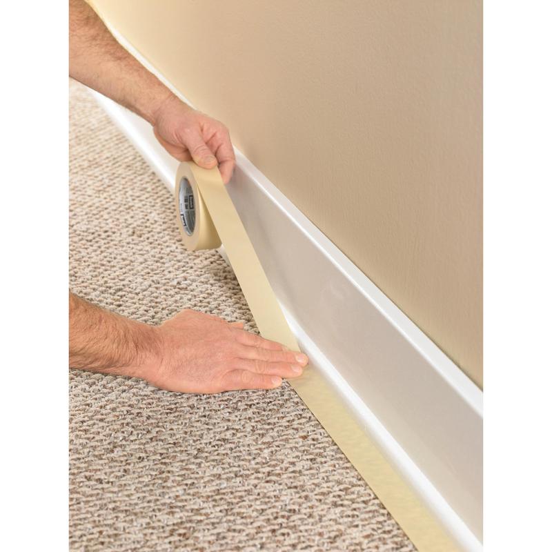 A person uses the Scotch® Classic Masking Tape (36 mm x 50 m, 1 roll/package, 70% PEFC) from 3M Deutschland GmbH to tape the edge of a white baseboard on light brown carpet before painting the beige wall above.