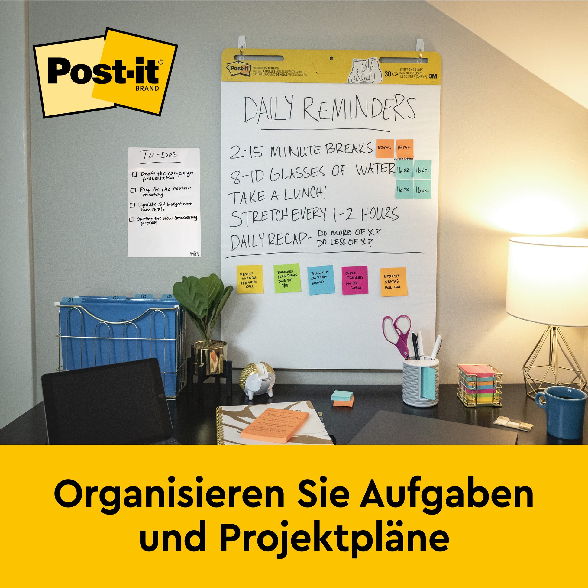 Ein Schreibtisch mit Büromaterial, Lampe, Haftnotizen und einem Stuhl. An der Wand: eine 3M Post-it® Super Sticky Recycling Meeting Chart (63,5x76,2cm), beschriftet mit "Daily Reminders". Deutscher Text: "Organisieren Sie Aufgaben und Projektpläne.