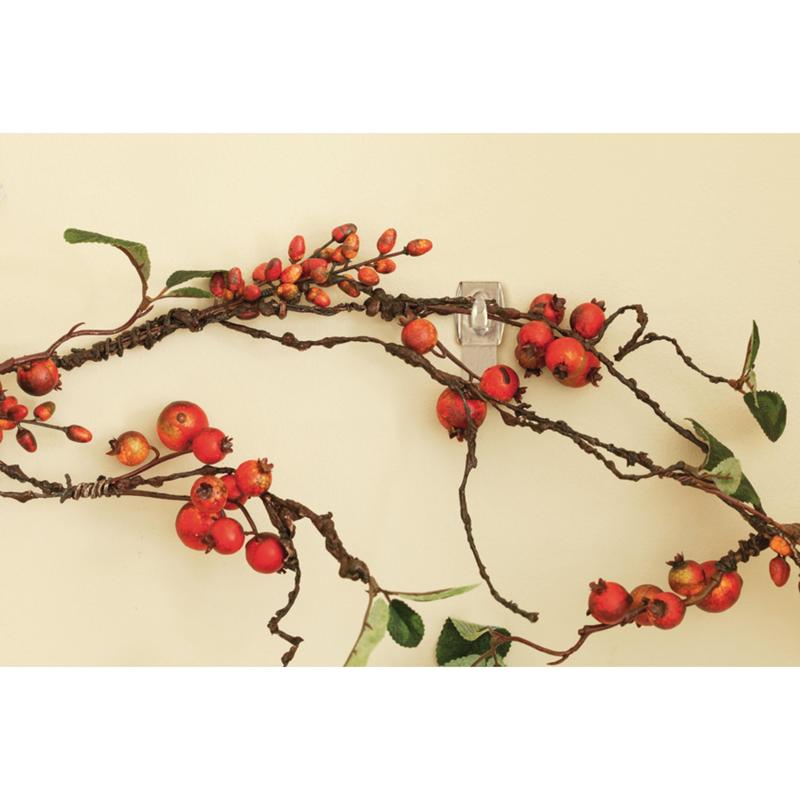 A decorative branch with red berries and green leaves hangs on a light wall, attached without a trace with the Command™ Mini Hook, transparent, with transparent strips (17006CLR) from 3M Deutschland GmbH.
