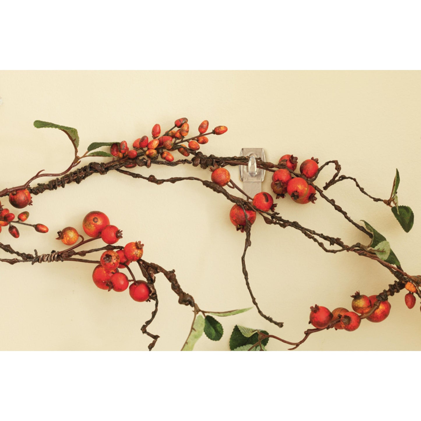 Ein dekorativer Zweig mit roten Beeren und grünen Blättern hängt an einer beigen Wand, getragen von dem Command™ Mini-Haken, transparent, mit transparenten Strips, 17006CLRFGN von 3M Deutschland GmbH - perfekte Aufbewahrung ohne Bohren.