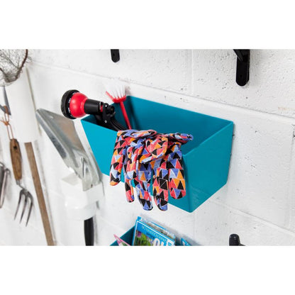 A pair of colorful garden gloves hangs over a blue bucket, which is attached to a white wall with Scotch-FIX™ Extreme double-sided outdoor mounting tape from 3M Deutschland GmbH. Inside the container are a spray nozzle and a cleaning brush, with garden tools hanging beside it.